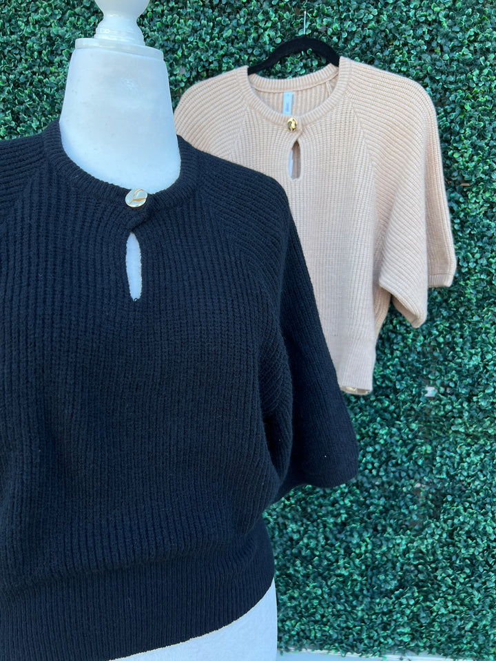 Two sweaters, one beige and one black, on a green textured surface.
