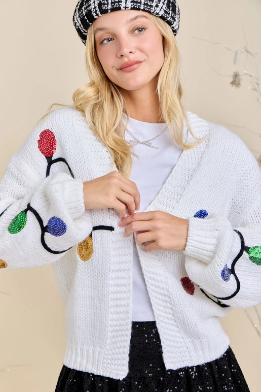 Woman wearing a white cardigan with colorful Christmas light design on a beige background