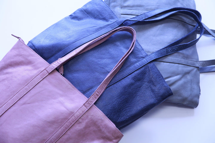 Three soft leather tote bags in blush pink, dusty blue, and light grey